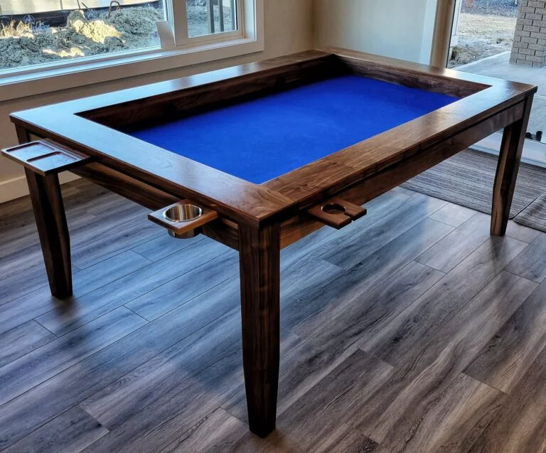 A table with a sunken middle surface for playing board games. sits in a living room with windows behind it, The table has cupholders and trays around the perimeter for holding drinks and game pieces