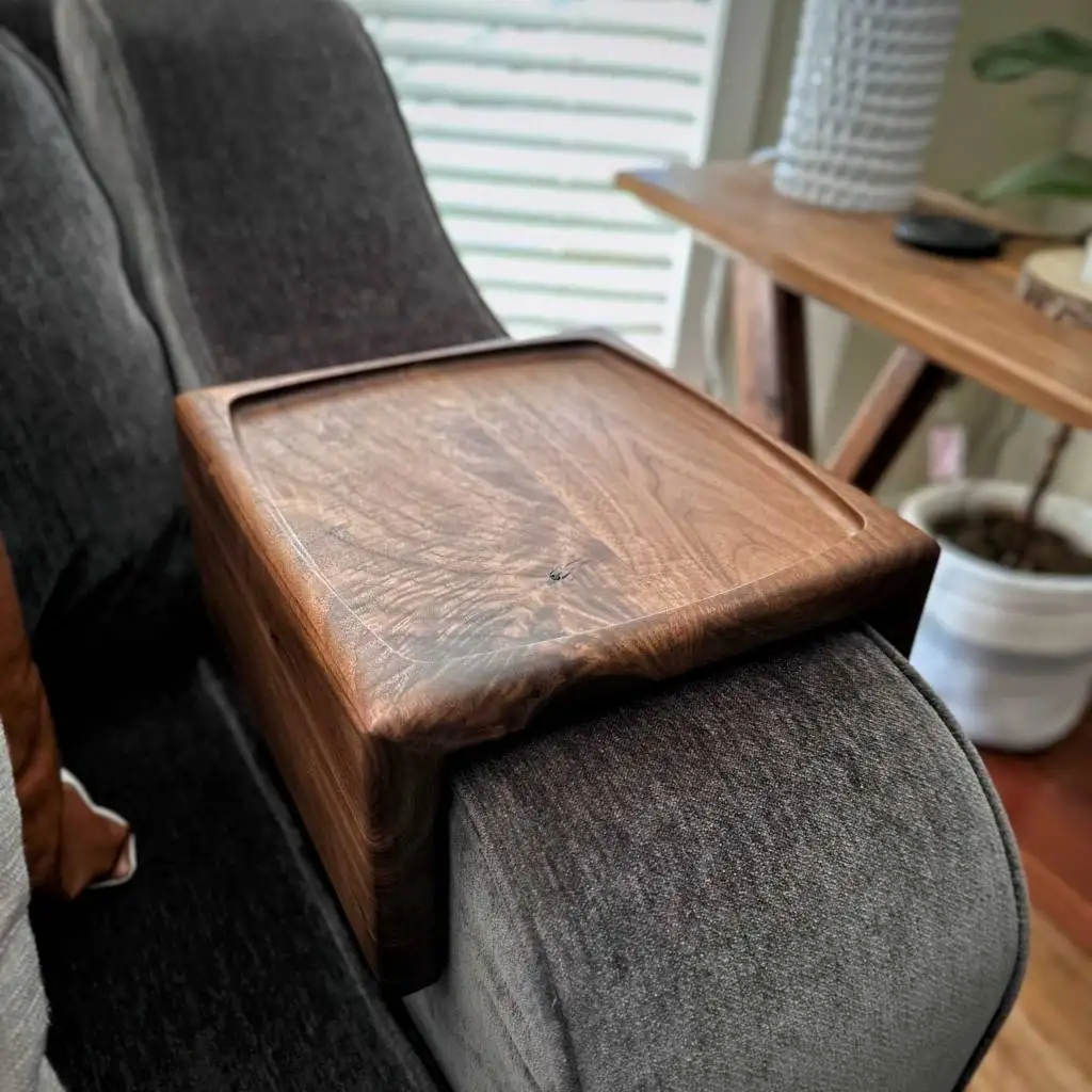 Couch table positioned over a sofa armrest, showcasing its recessed surface design and the beautiful figured grain pattern of the walnut wood